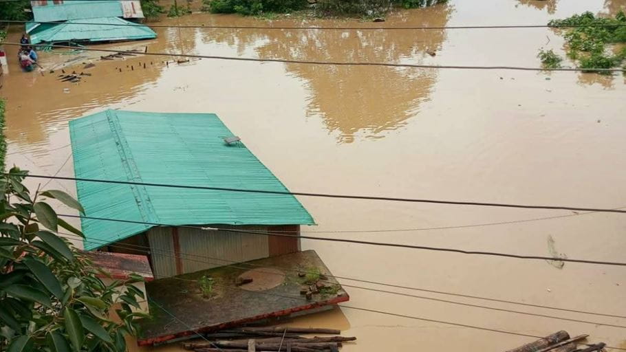Houses partially submerged in muddy floodwaters; power lines visible in the foreground.