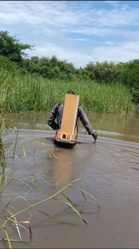 One of Tearfund’s nutrition officers walks through the deep floodwaters, carrying a height board on his back, one of the tools used to assess children for malnutrition.