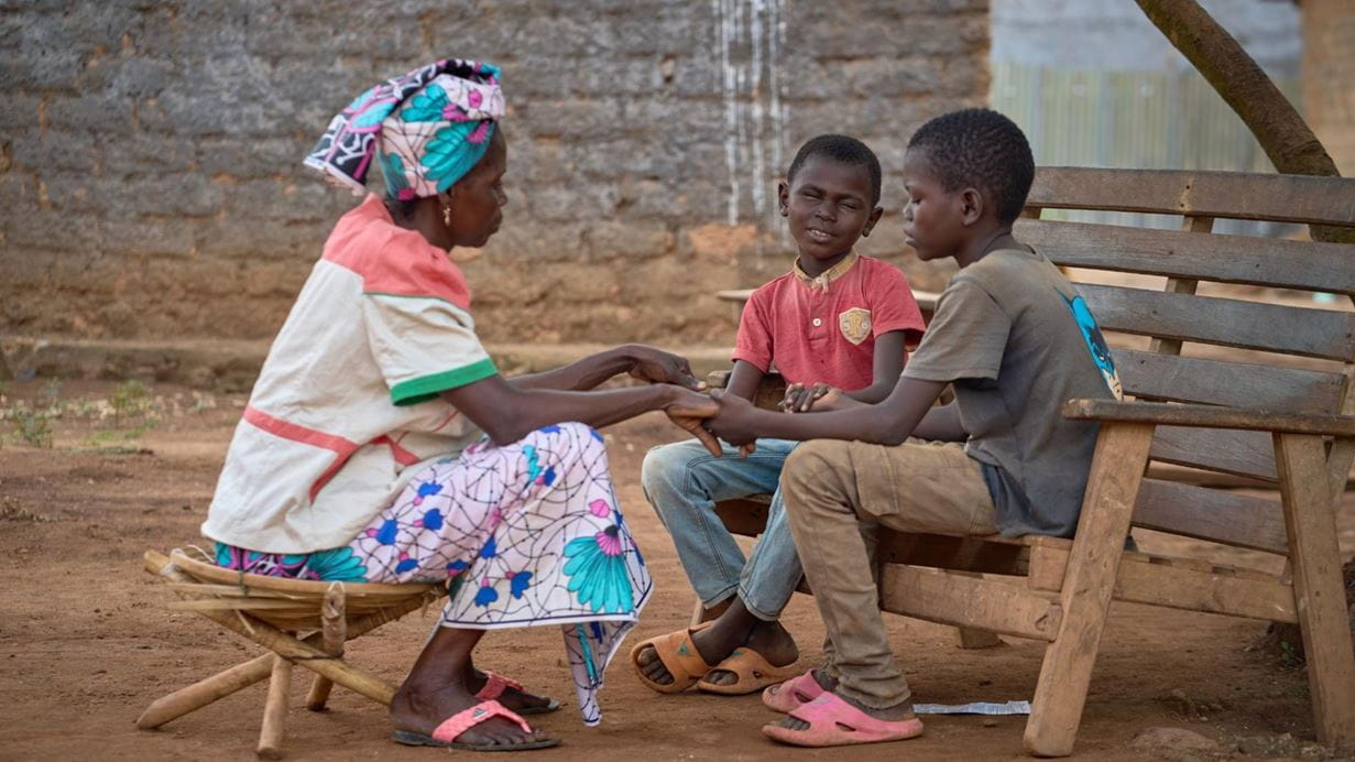 An older woman sitting and holding hands with two young boys sitting on a bench.