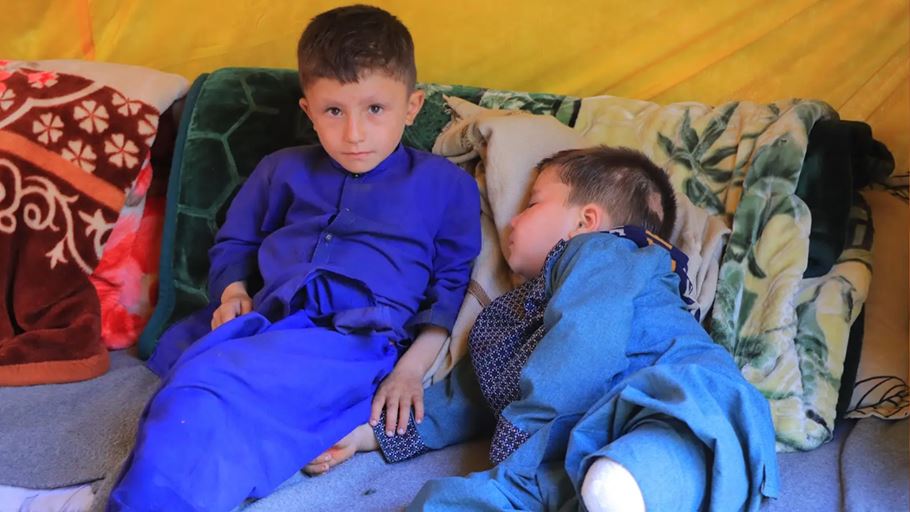 Two young boys rest on a blanket, one awake and alert, the other asleep.