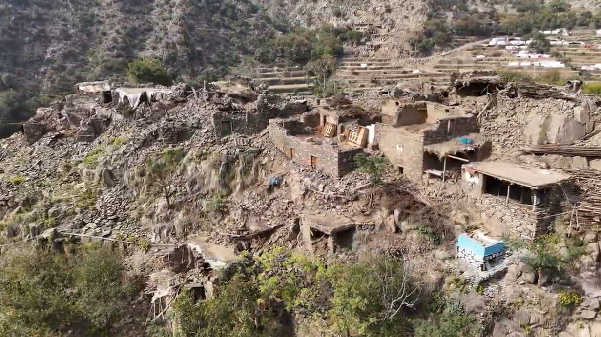 Aerial view of a village on a rocky hillside with terraced fields in the background.