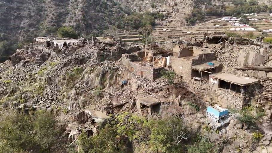 Aerial view of a village on a rocky hillside with terraced fields in the background.