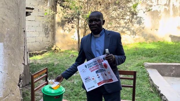 Man in suit disinfecting hands, holding Ebola prevention flyer outside.