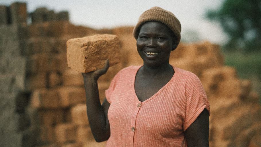 Mary smiles as she holds up one of the bricks that she has made.