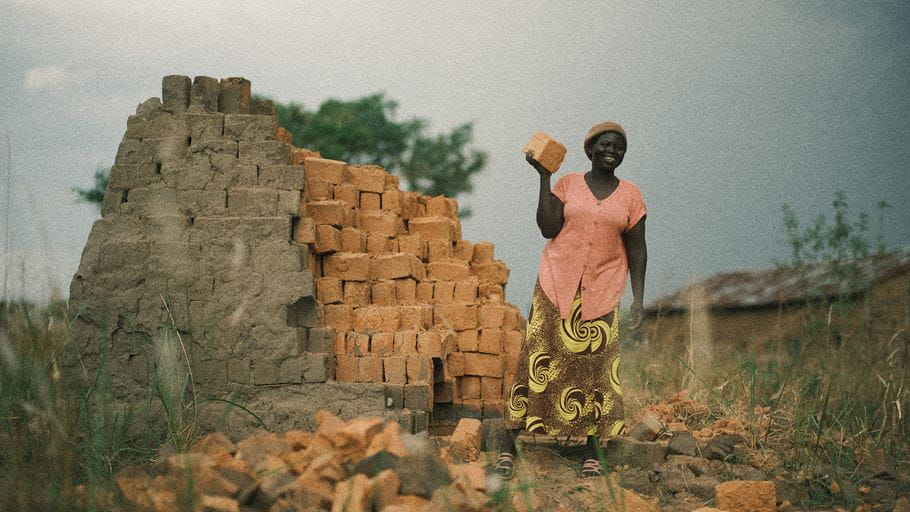 Mary in Kajo-Keji stands with a pile of the bricks she has made.