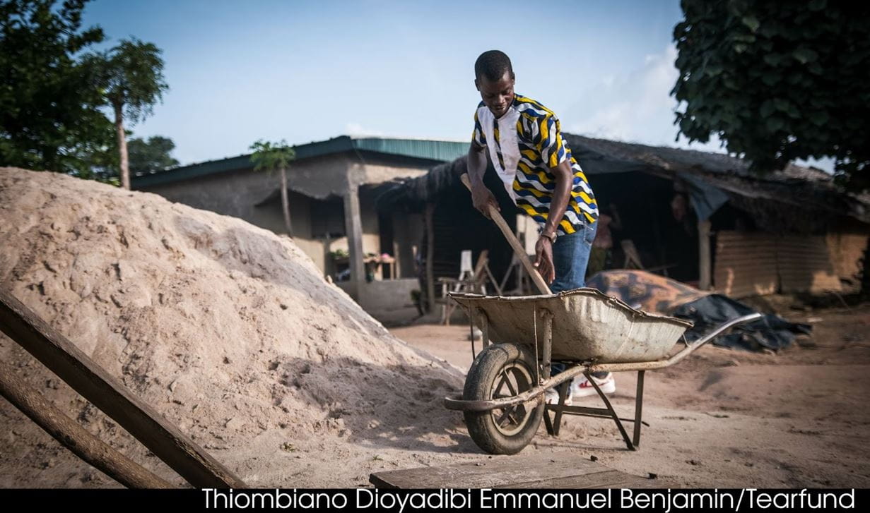 A man stands next to a heap of sand, moving the sand to a wheelbarrow