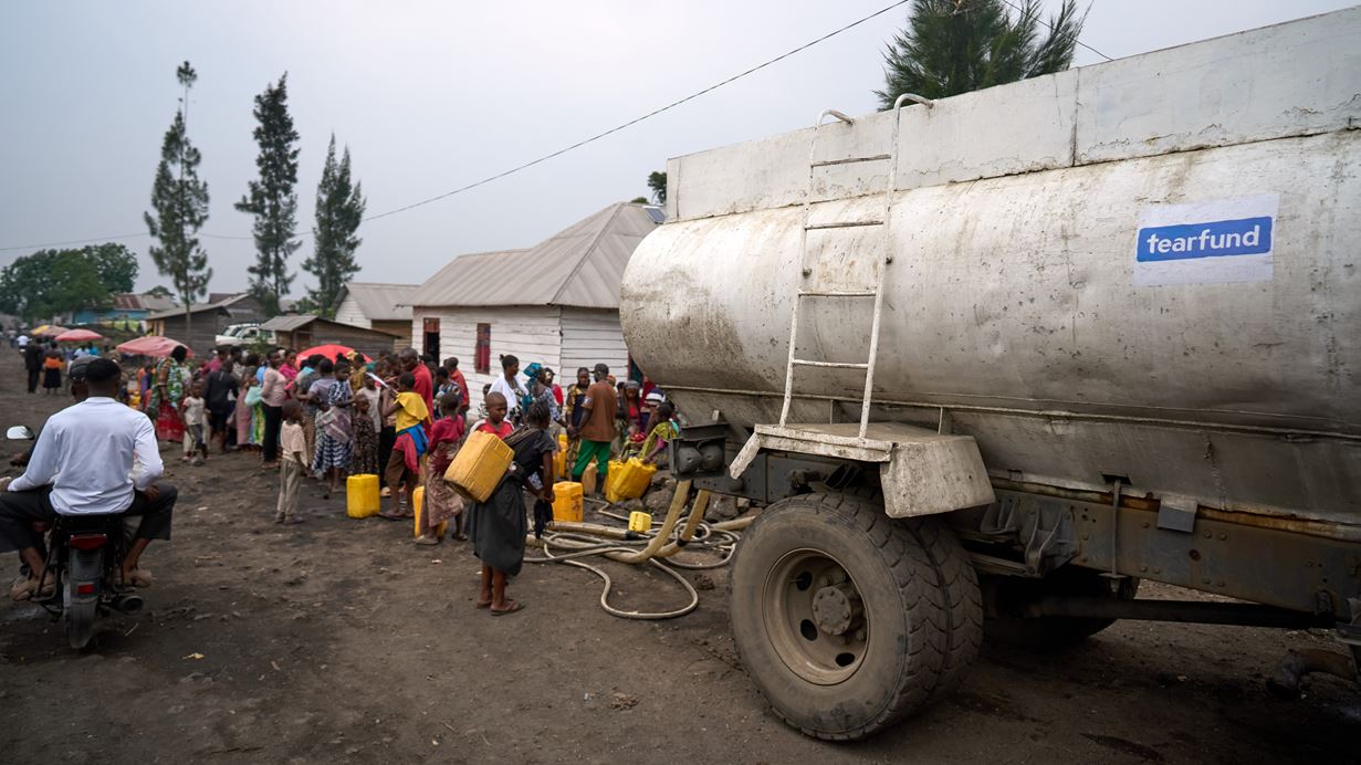 A large tanker with a Tearfund logo delivers clean water to a queue of people in DRC