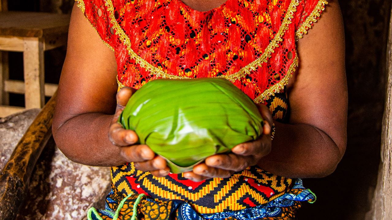 A close-up of someone holding the food wrapped in banana leaves