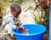 A child washing their hands in a large tub of clear water